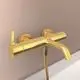 Wassertapete in gebürstetem Gold von Ideal Standard, mit einem gesamten Verbindungsrohr und einem schlanken Wasserhahn, montiert an einer hellen Wand.